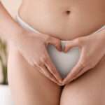 Young woman in panties making heart shape with hands at home